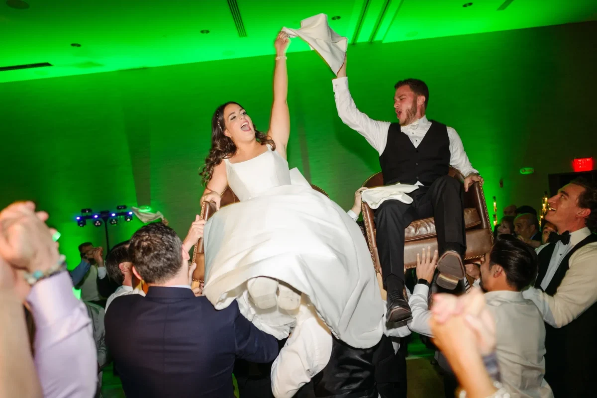 Bride and groom being held up by people on dance floor with green wedding uplighting in the background