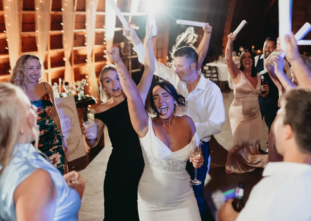 Packed dance floor with glow sticks and wedding guests with arms up in the air